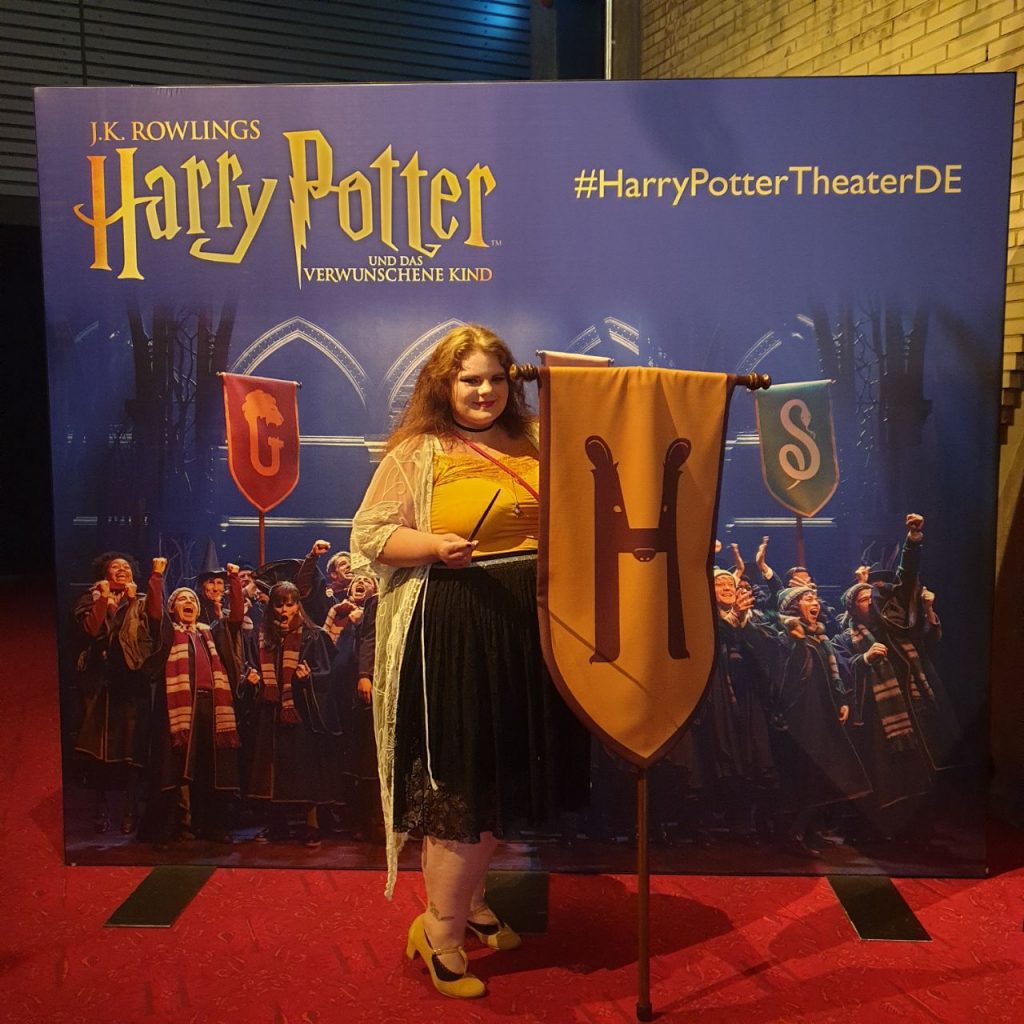 Bunmom im Hufflepuff-Look mit Zauberstab vor Harry Potter-Plakat